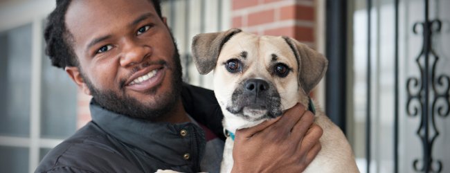 dog owner holds his dog in front of brick house