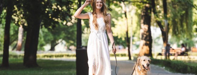 woman in white dress walking dog on a leash down the sidewalk