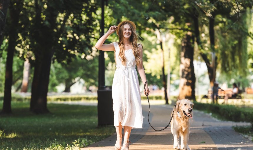 woman in white dress walking dog on a leash down the sidewalk