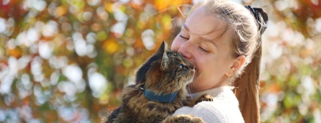 Mujer abrazando un gato marrón con un localizador gps en el collar al aire libre, con un árbol en el fondo